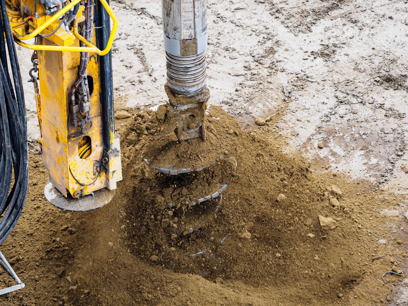 Auger drilling into soil beside a yellow drilling rig